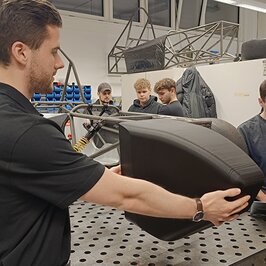 Student hält ein Stück der Fahrzeughülle an das Gerüst