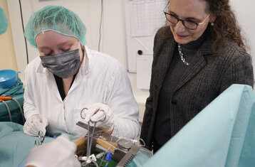 Zwei Personen in Ärztekittel beim operieren während eine weitere Frau zuschaut