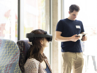 Eine Frau trägt eine VR Brille und sitzt in einem Bahnsessel.