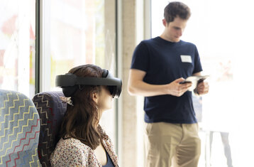 Eine Frau trägt eine VR Brille und sitzt in einem Bahnsessel.