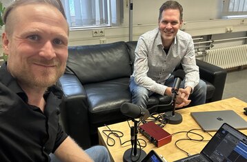 Two people sitting at a table with recording equipment. 