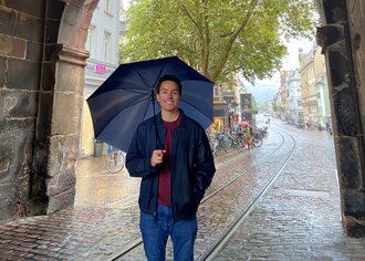 [Translate to English:] Ein Junge mit einem Regenschirm in einem Torbogen