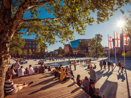 You see people sitting in the Old Synagogue Square in Freiburg