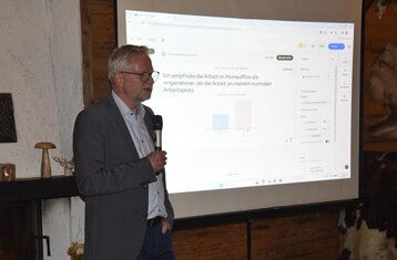 Man sieht einen Mann mit Mikrofon vor einer Leinwand stehen