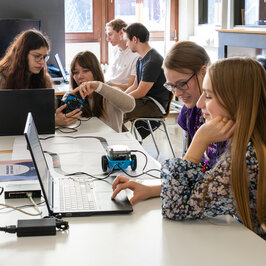 Mehrerer Jugendliche sitzen an Laptops, und programmieren einen Roboter