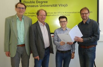 Vier Herren der zweite von rechts hält eine Auszeichnung in der Hand