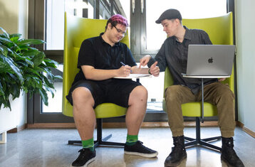 Man sieht zwei Jugendliche in grünen Sesseln sitzen und etwas aufschreiben