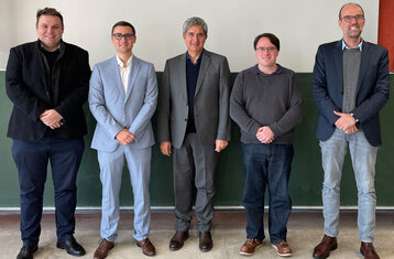 You see five men standing in a row and smiling into the camera