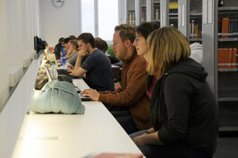 Viele lernende Studierende an einem langen Tisch in der Bibliothek