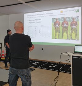 Personen betrachten eine Folie, die per Beamer an einer Wand präsentiert wird