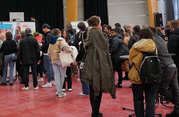 Man sieht viele Studierende die sich an Ständen mit Rollups informieren