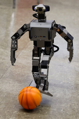 Ein kleiner silberner Roboter läuft auf einen orangenen Ball zu