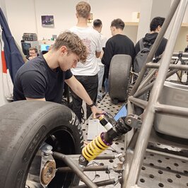 Ein Student schaut neben dem Rennwagengestänge in einen Bildschirm