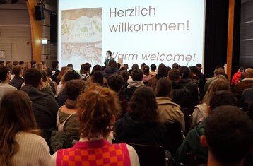 Man sieht eine Frau die vor einer Menschenmenge spricht