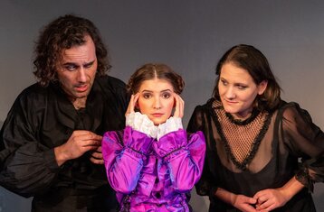 Drei Schauspieler zwei Frauen ein Mann, die Frau in der Mitte trägt pink