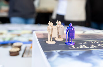 Symbolbild: Spielfiguren im Vordergrund im Hintergrund zwei unscharfe Personen