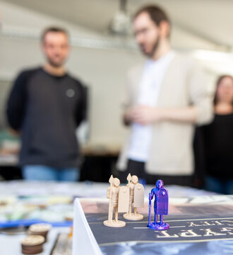 Symbolbild: Spielfiguren im Vordergrund im Hintergrund zwei unscharfe Personen