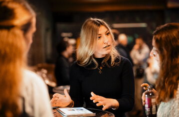 Three woman standing at a table speaking to each other