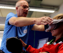 Ein Mann kontrolliert die VR-Brille eines Jungen auf den richtigen Sitz