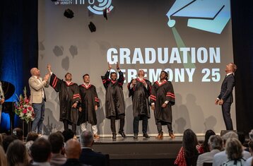 Graduierende auf der Bühne werfen ihre Hüte in die Luft