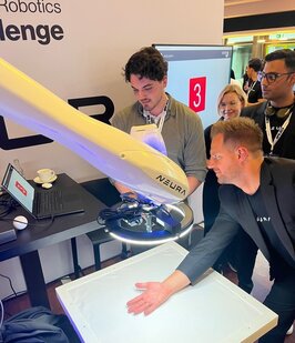  A man places his hand in front of the robot arm at a project stand. 