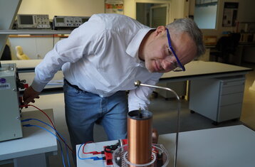 Man sieht einen Mann der eine Spule anschaut, er trägt ein Schutzbrille