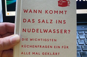 Eine Hand hält das beschrieben Buch hoch
