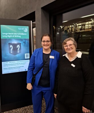 Zwei Personen vor dem Plakat der Veranstaltung