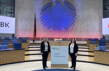 Man sieht zwei Frauen sie stehen neben einem Rednerpult