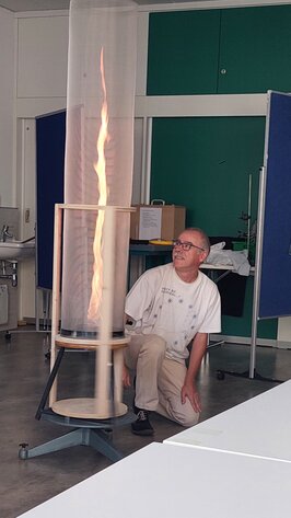 A man kneeling next to a glass container in which a pillar of fire is blazing