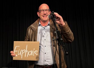 Prof. Selke hält ein Schild in der Hand mit der Aufschrift "Euphorie"
