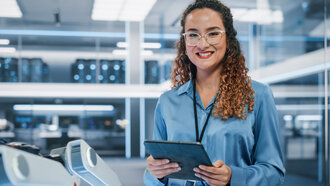 Portrait of a Beautiful Hispanic Female Wearing Glasses, Using Tablet Computer, Looking at Camera and Smiling. Businesswoman, Information Technology Manager, Robotics Engineering Specialist. Eine junge Frau lächelt in die Kamera, sie hält ein Tablet in der Hand