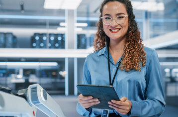 A young woman smiles at the camera, holding a tablet in her hand 
