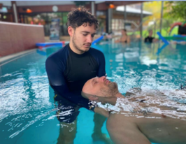 Ein Mann steht in einem Schwimmbecken und hält sanft den Kopf eines Patienten